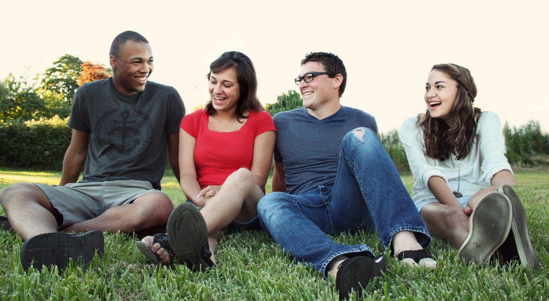 smiling women and men sitting on green grass